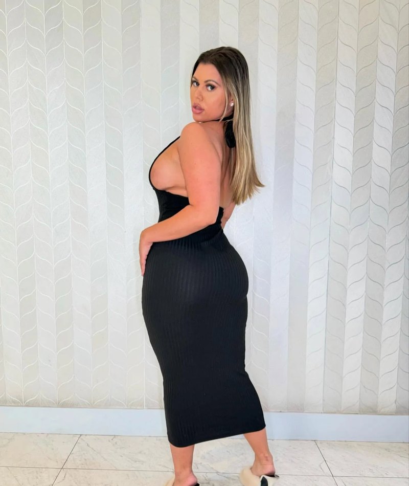 Milani wearing a fitted black dress against a patterned white wall