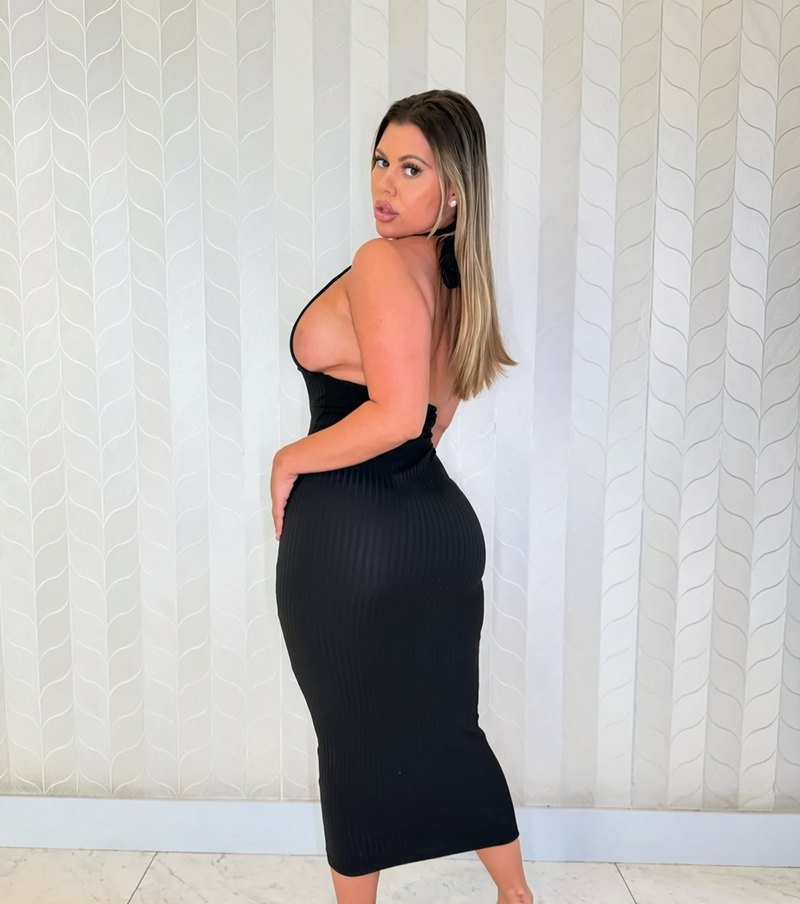 Milani wearing a fitted black dress against a patterned white wall